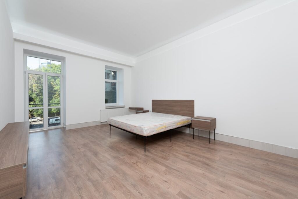 Spacious minimalist bedroom featuring wooden floors and large windows for natural light.